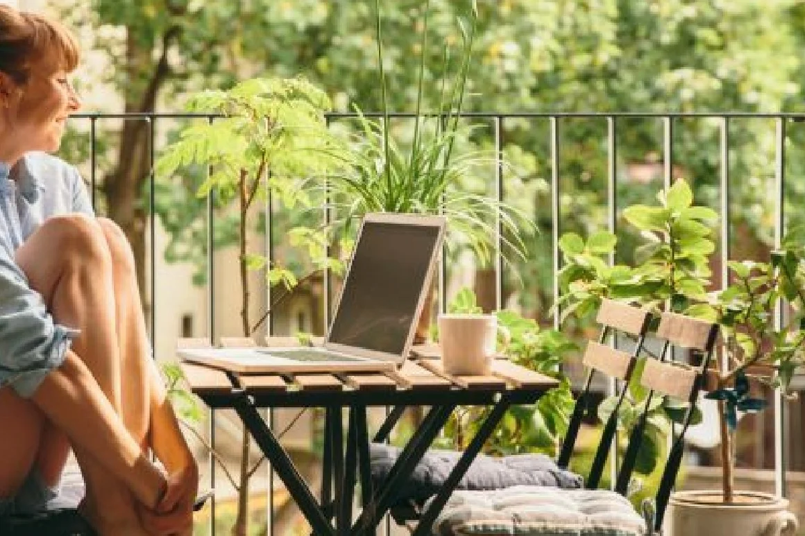 Person sitzt auf Balkon und arbeitet am Laptop.